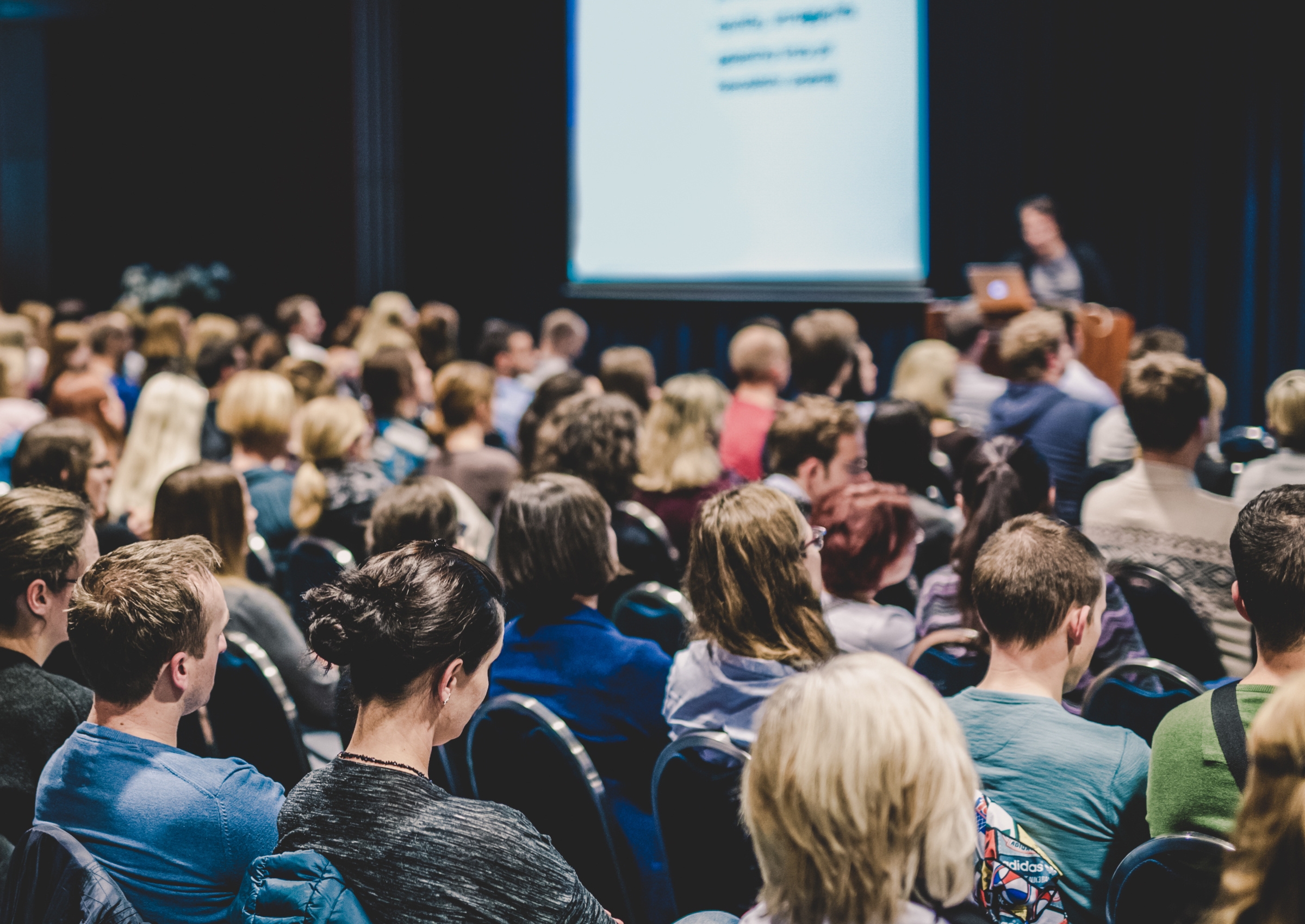 In einem dicht besetzten Konferenzraum sitzen zahlreiche Menschen und hören einem Vortrag zu